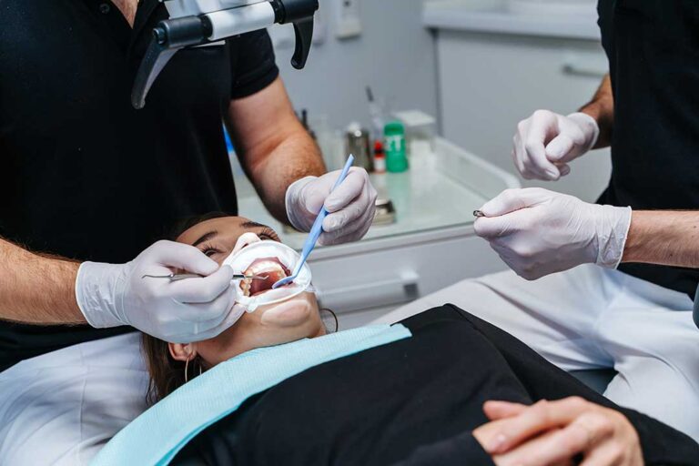 Adult gently brushes teeth at a bathroom sink with a soft toothbrush and fluoride toothpaste.
